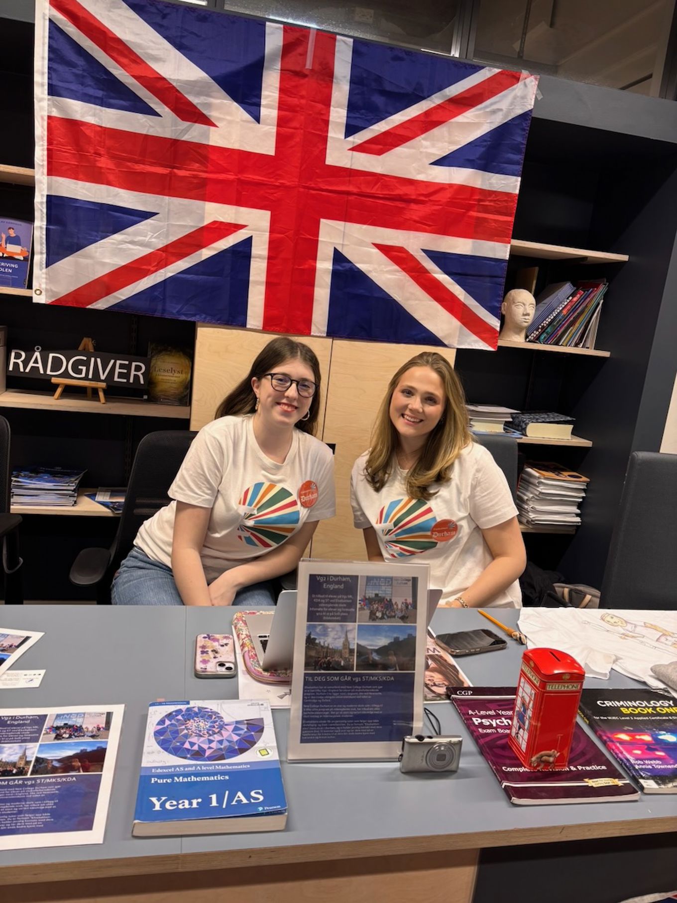 et par personr som sitter ved et skrivebord med bøker og et flagg bak seg et par personr som sitter ved et skrivebord med bøker og et flagg bak seg