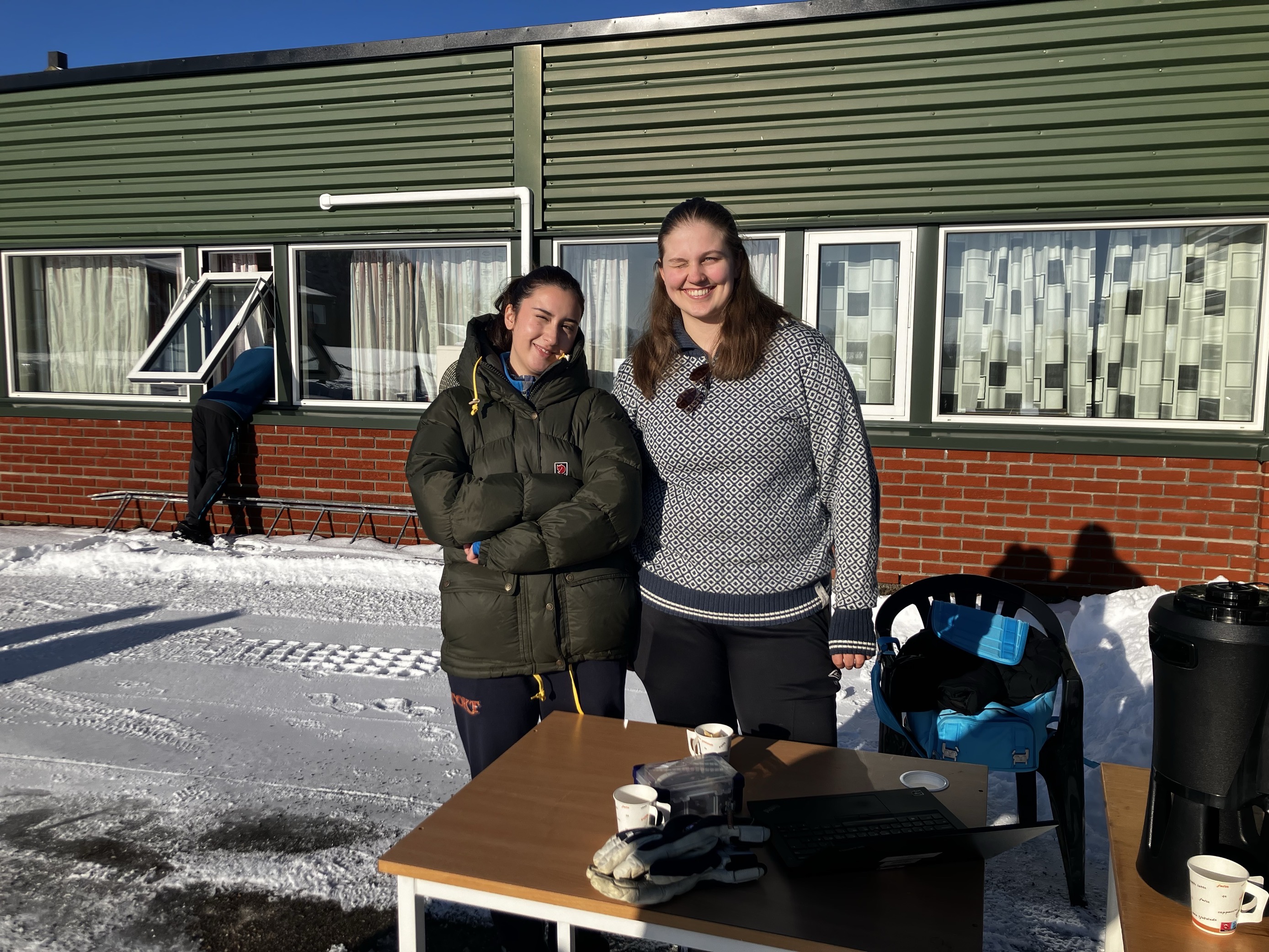 Foto: Jack Bonsak et par personr som står ved siden av et bord med en snødekt bygning i bakgrunnen