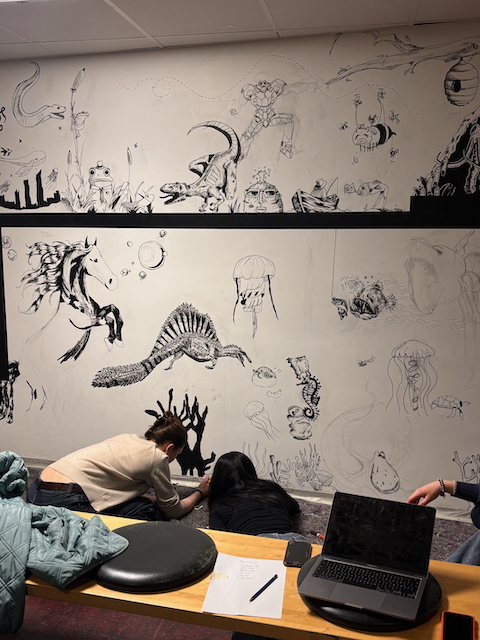 En gruppe mennesker som sitter ved et bord med en bærbar datamaskin og tegninger på veggen