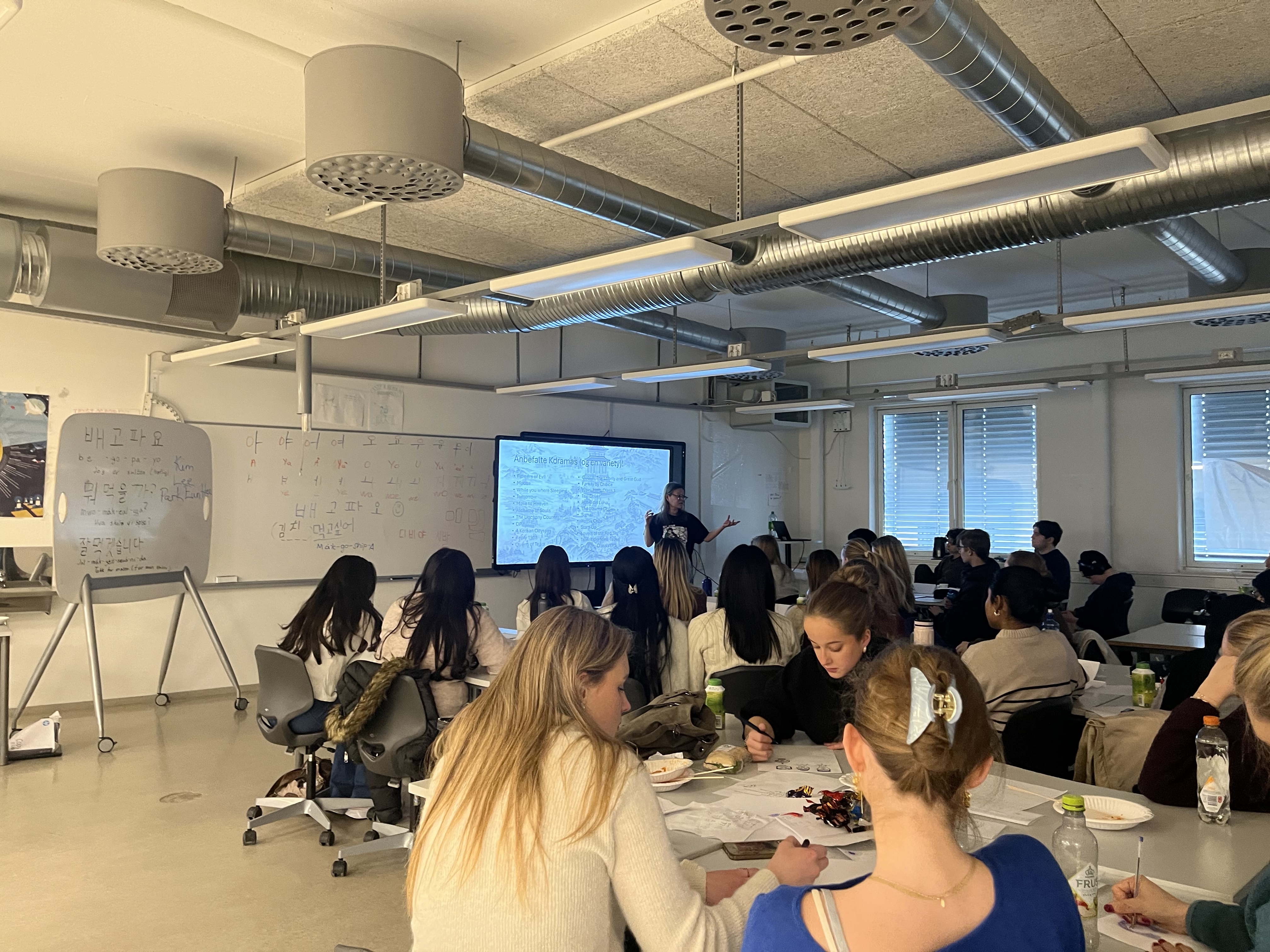 en gruppe mennesker som sitter ved bord i et rom med en stor skjerm