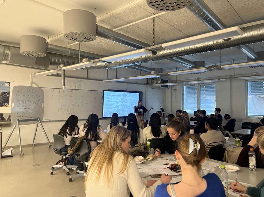 en gruppe mennesker som sitter ved bord i et rom med en stor skjerm