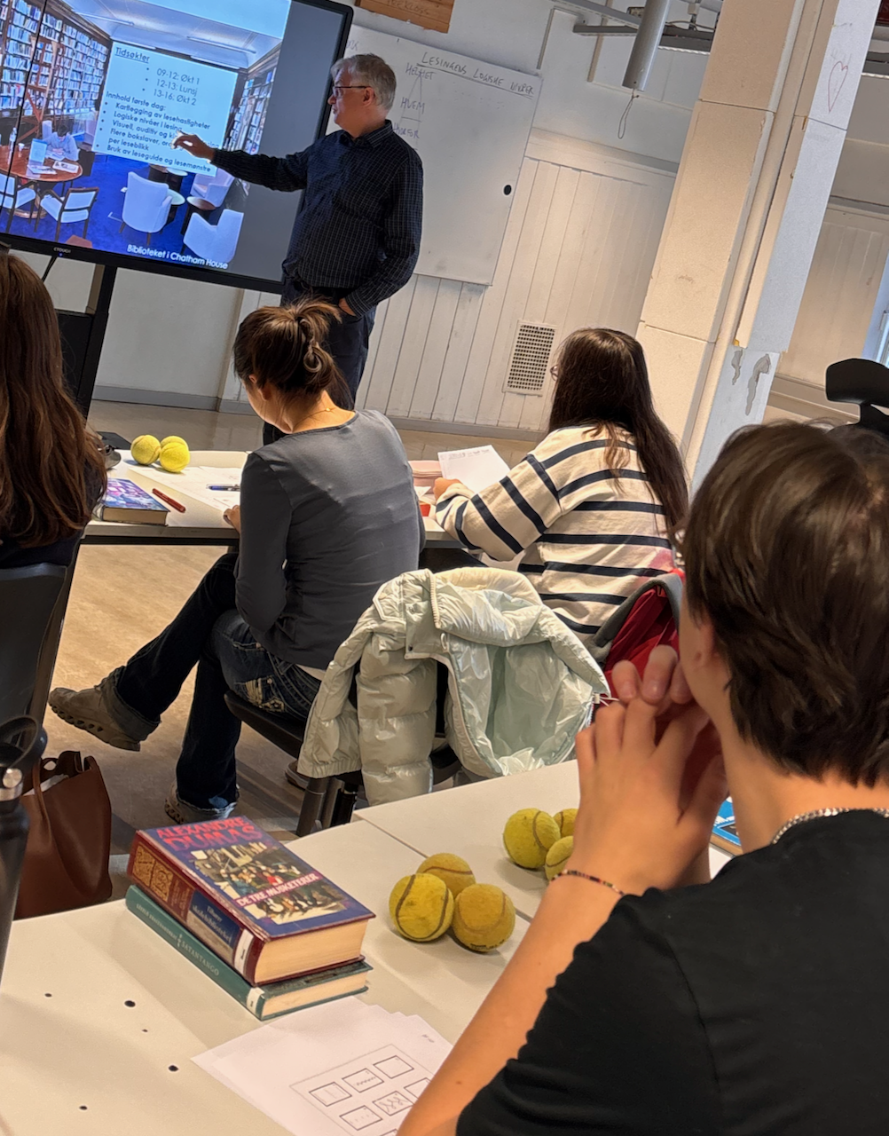 en gruppe mennesker som sitter ved et bord og ser på en person som snakker