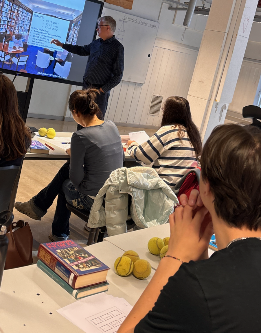 en gruppe mennesker som sitter ved et bord og ser på en person som snakker en gruppe mennesker som sitter ved et bord og ser på en person som snakker