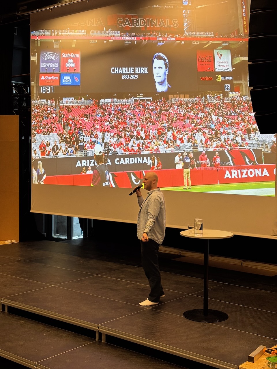 en person som står på en scene med en mikrofon foran en stor skjerm