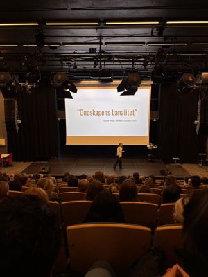 En person på en scene med en projektorskjerm foran et publikum