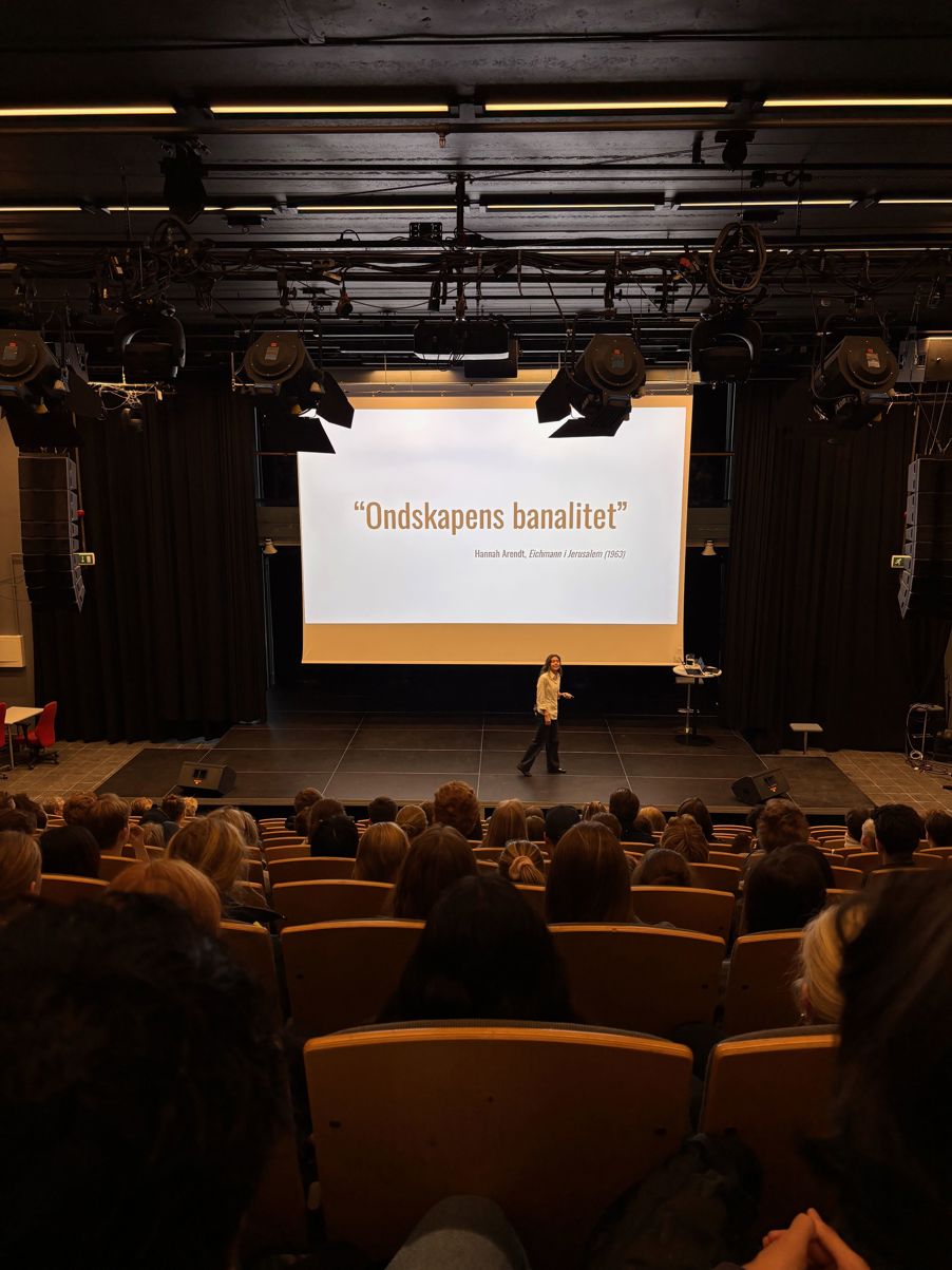 En person på en scene med en projektorskjerm foran et publikum