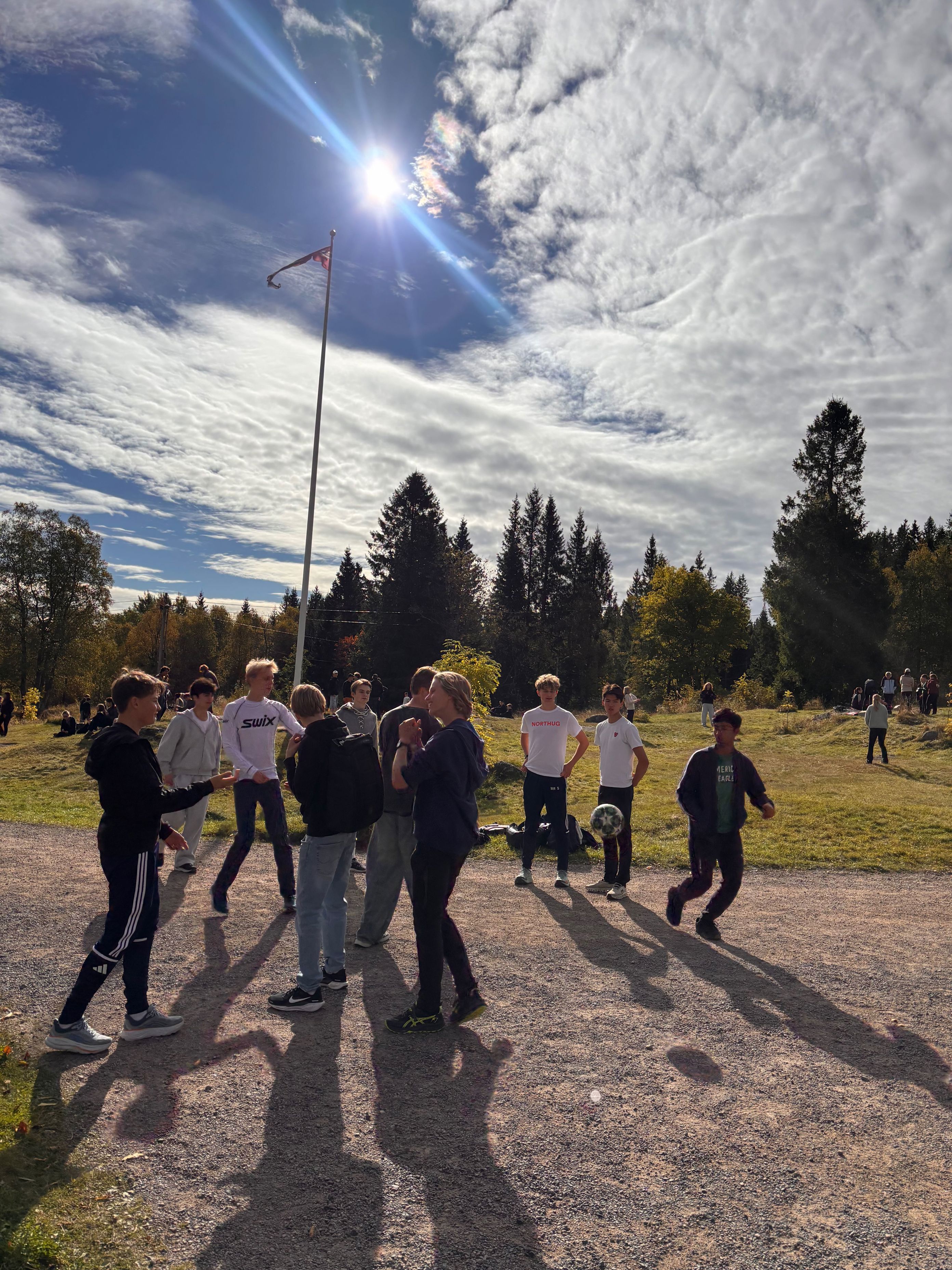 En gruppe mennesker som står på en grusvei med et flagg og trær i bakgrunnen