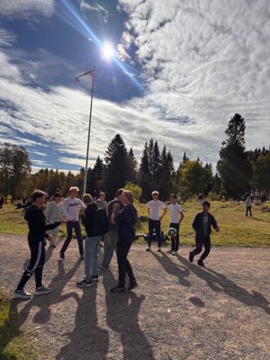 En gruppe mennesker som står på en grusvei med et flagg og trær i bakgrunnen