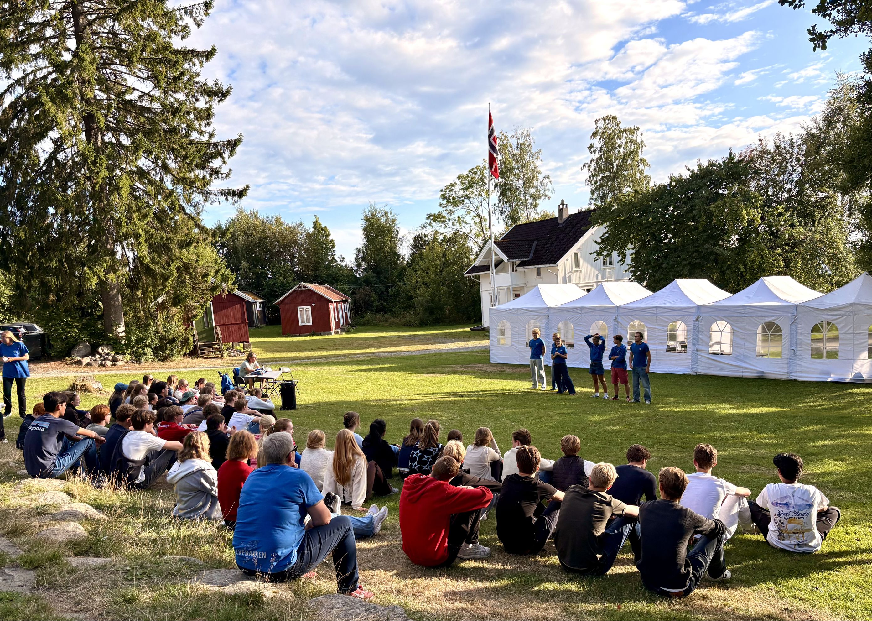 En gruppe mennesker som sitter på gresset foran et telt