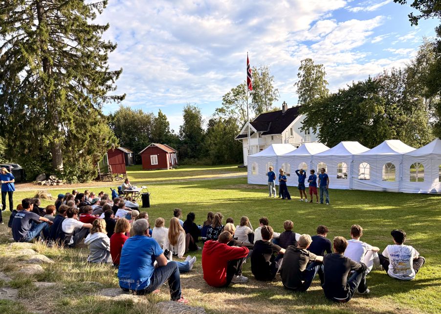 En gruppe mennesker som sitter på gresset foran et telt